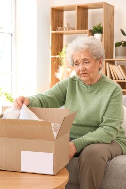 Evde paket açan yaşlı bir kadın.