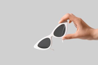 Beyaz arka planda şık güneş gözlüğü tutan kadın.