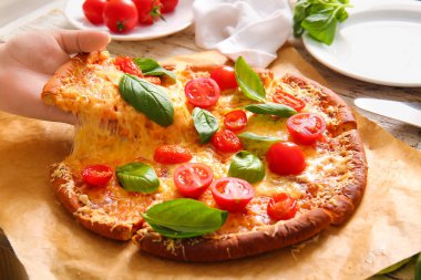 Kadın eli, parşömen üzerinde lezzetli bir pizza margaritası alıyor, yakın plan.