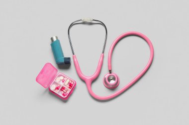 Astım spreyi, steteskop ve gri arka planda bir kutu hap.