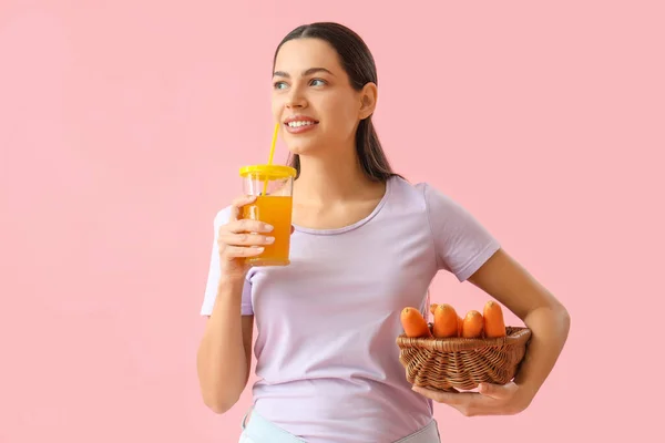 粉红背景的年轻女子 一杯蔬菜汁和胡萝卜 — 图库照片