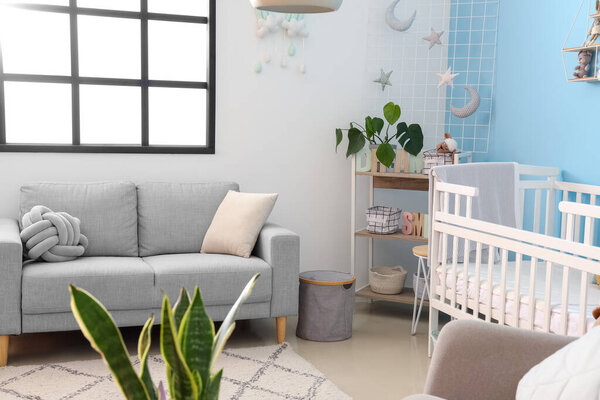 Interior of stylish bedroom with baby crib, sofa and shelving unit