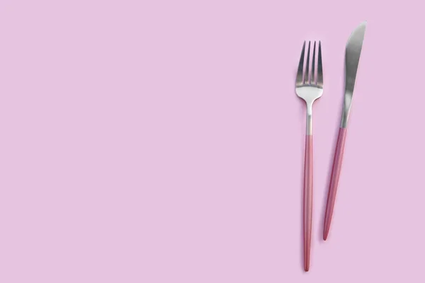 ピンクの背景にステンレス製のフォークとナイフ — ストック写真
