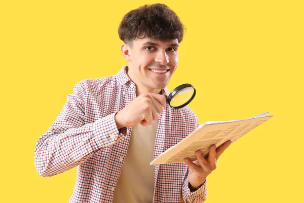 黄色の背景に拡大鏡と新聞を持つ若い男 — ストック写真