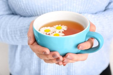 Beyaz duvarın yanında bir fincan papatya çayıyla güzel genç bir kadın.