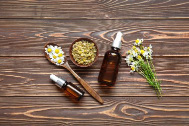 Gerekli yağ şişeleri, taze ve kurumuş papatya çiçekleri ahşap arka planda.