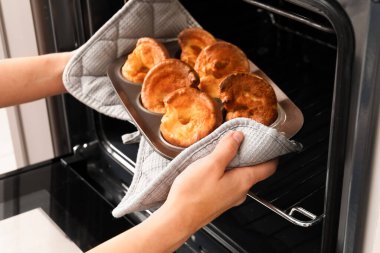Mutfaktaki fırından lezzetli Yorkshire pudingiyle yemek pişiren kadın.