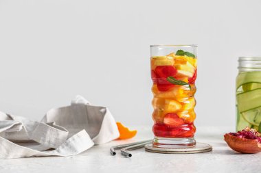 Beyaz masada farklı dilimlenmiş meyvelerle dolu cam ve mason kavanozu.