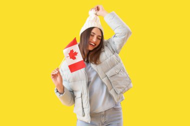 Sarı arka planda Kanada bayrağı olan sıcak şapkalı genç bir kadın.