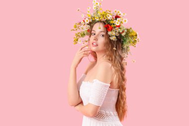 Pembe arka planda çiçek çelengi giymiş güzel bir kadın. Yaz gündönümü