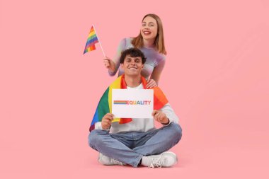 Kelime eşitliği ve pembe arka planda LGBT bayrakları olan genç bir çift ellerinde kağıt tutuyor.