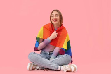 Pembe arka planda oturan LGBT bayrağıyla genç bir kadın.