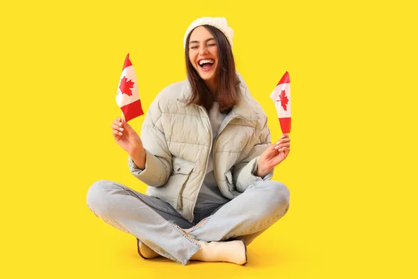 头戴暖帽 头戴加拿大国旗的年轻女子坐在黄色背景上 — 图库照片