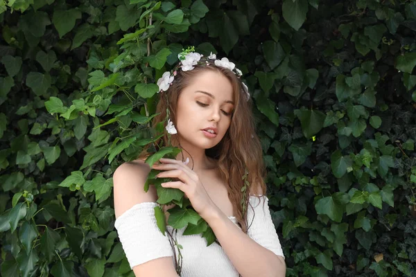 緑のツタの屋外近くの彼女の髪に花を持つ美しい若い女性 — ストック写真