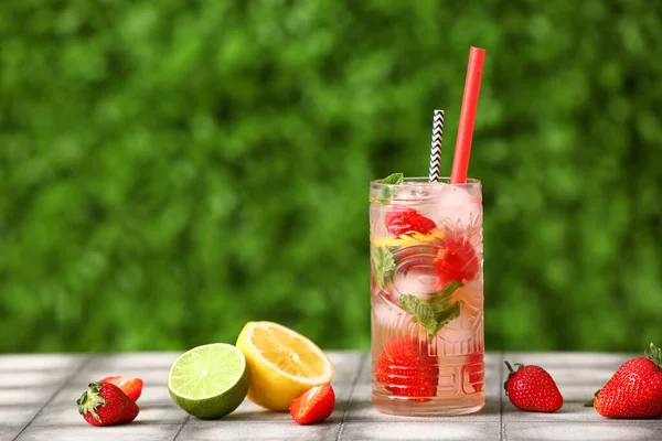 Glass of strawberry lemonade on grey tile table outdoors