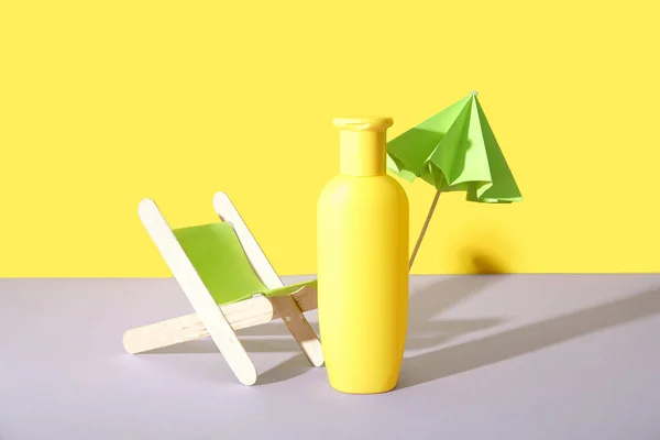 黄色の壁の近くにライラックテーブルの上にミニチュアデッキチェアと日焼け止めクリームのボトルと創造的な組成物 — ストック写真