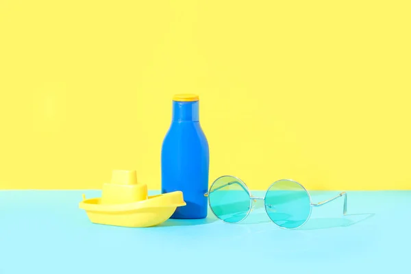 Fles Zonnebrandcrème Met Zonnebril Speelgoedschip Blauwe Tafel Nabij Gele Muur — Stockfoto