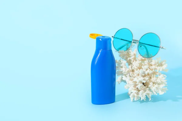 Bottle of sunscreen cream with sunglasses and coral on blue background