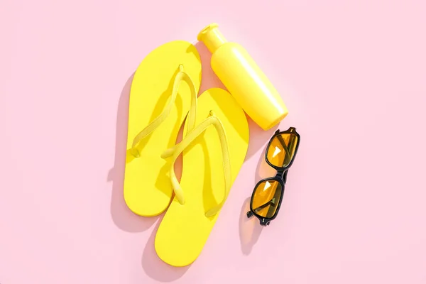 stock image Bottle of sunscreen cream with sunglasses and flip flops on pink background