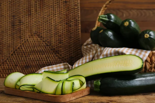 Weidenkorb Mit Vielen Frischen Zucchini Und Scheiben Auf Holzgrund — Stockfoto