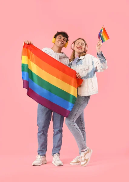 ピンクの背景にLgbtの旗を持つヘッドフォンで若いカップル — ストック写真