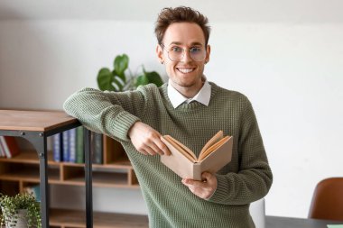 Genç adam kütüphanede kitap okuyor.