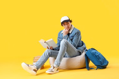 Erkek öğrenci sarı arka plan üzerine kitap okuyor.