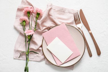 Boş davetiye kartı, çatal bıçak takımı ve karanfil çiçekleri beyaz masada.