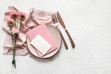 Boş davetiye kartı, çatal bıçak takımı ve karanfil çiçekleri beyaz masada.