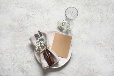Boş davetiye kartı, çatal bıçak takımı ve beyaz masadaki çigila çiçekleriyle temiz tabak.