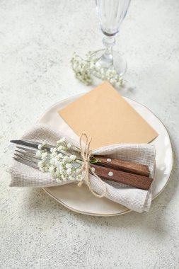 Boş davetiye kartı, çatal bıçak takımı ve beyaz masadaki çigila çiçekleriyle temiz tabak.