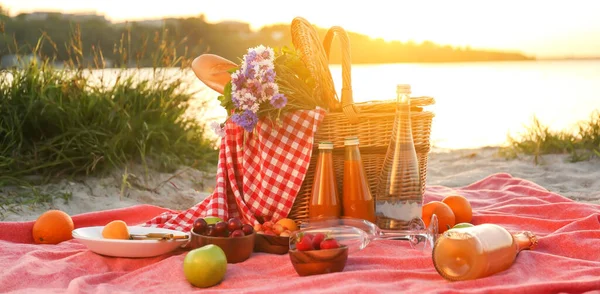 有美味食物和饮料的柳条篮 在河边举行浪漫野餐 — 图库照片