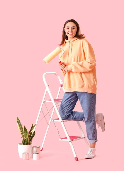 塗装ローラー はしご 缶やピンクの背景に観葉植物を持つ若い女性 — ストック写真