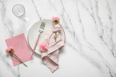 Boş davetiye kartı, çatal bıçak takımı ve karanfil çiçekleri beyaz masada.