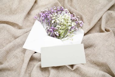 Zarfın içinde güzel çigila çiçekleri ve buruşmuş gri masa örtüsünün üzerindeki boş davetiye kartı.