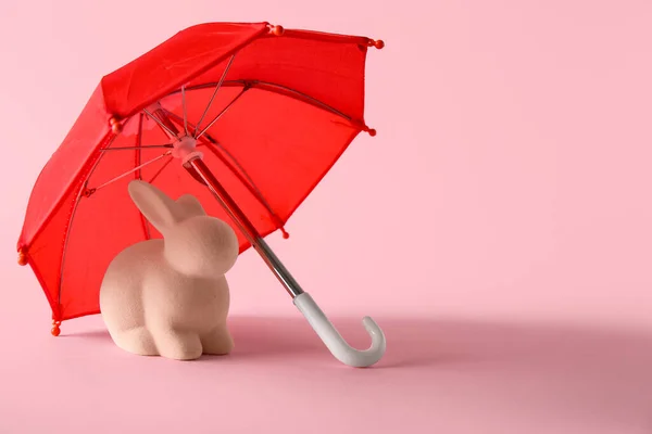 Creative composition with rabbit toy and red mini umbrella on pink background
