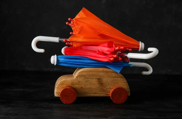 Creative composition with wooden toy car and mini umbrellas on black background. Insurance concept