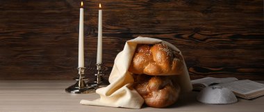 Traditional challah bread with Jewish cap, Torah and candles on wooden background clipart