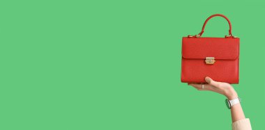 Şık kol saati ve kırmızı çantalı, yeşil arka planda, metin için yeri olan bir kadın el.