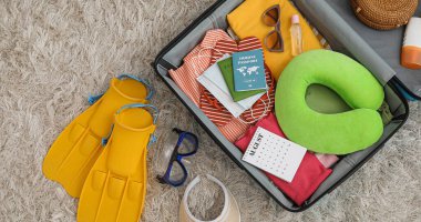 İçinde eşyalar, pasaportlar, takvim ve plaj aksesuarları olan valizi aç.