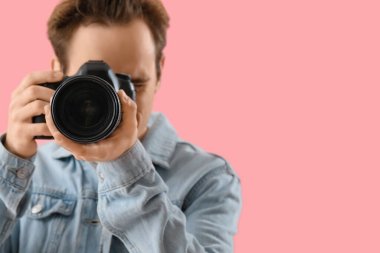 Pembe arka planda modern kameralı genç bir erkek fotoğrafçı.