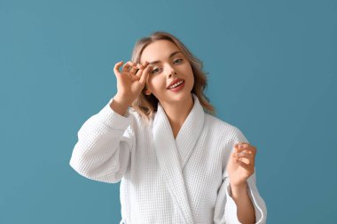 Mavi arka planda yüz geliştirme egzersizi yapan genç bir kadın.