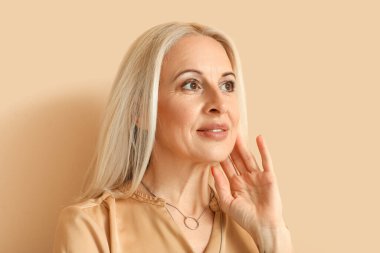Mature blonde woman on beige background, closeup