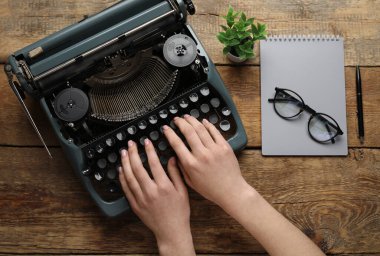 Kahverengi ahşap arka planda daktilo, gözlük, defter ve çiçekle daktilo kullanan kadın.