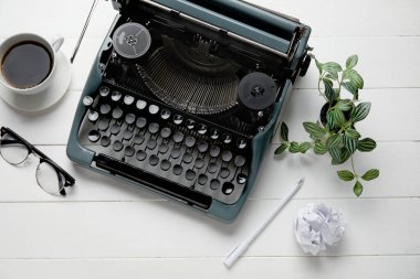 Beyaz ahşap arka planda kahve, gözlük ve çiçekli klasik daktilo.