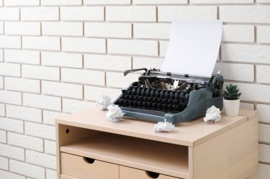 Tuğla duvarın yanındaki masa üzerinde buruşuk kağıt ve çiçekli klasik daktilo.