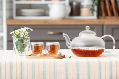 Çaydanlıklı ahşap tepsi, mutfaktaki masada papatya çayı ve çiçekler.