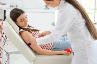 Kadın doktor klinikte genç bir donörü kan nakline hazırlıyor.