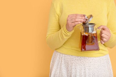 Sarı duvarın yanında çaydanlık papatya çayıyla güzel genç bir kadın.