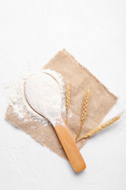 Tahta kaşık, beyaz arka planda un ve buğday kulakları.